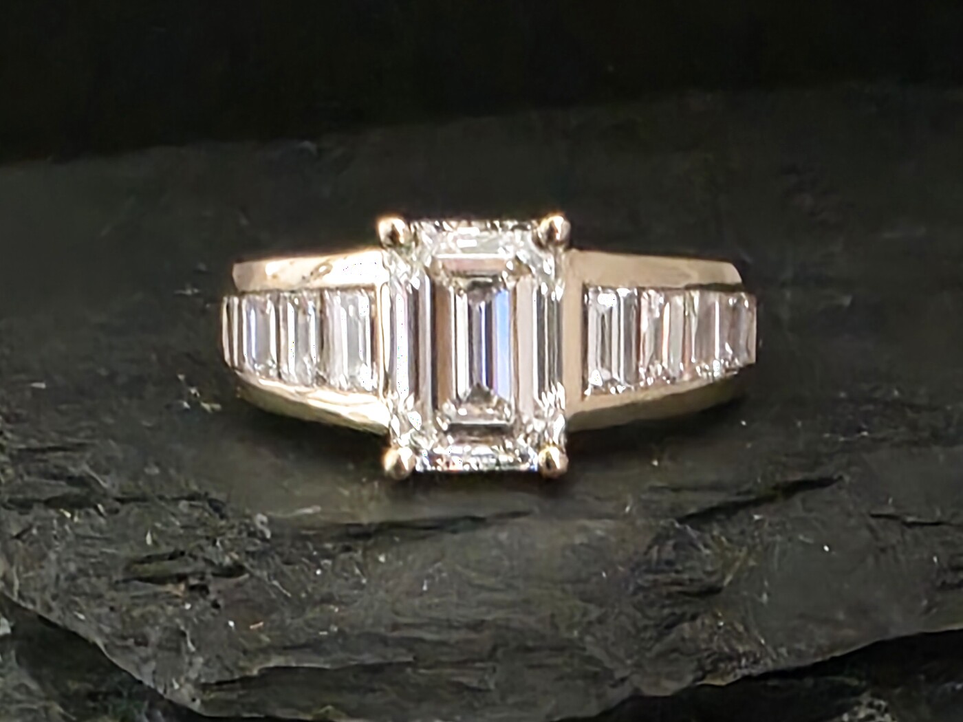Emerald-cut diamond engagement ring with channel-set baguette shoulders in yellow gold